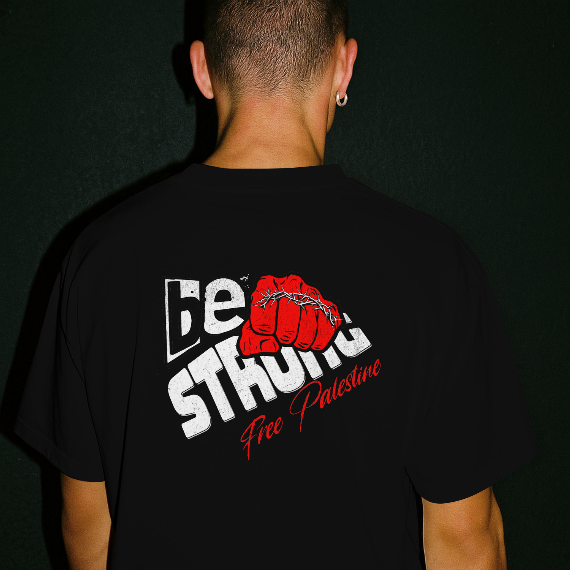 Back view of a person wearing a black T-shirt with a bold red fist graphic and “Be Strong – Free Palestine” text design printed on the back.